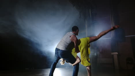 Zoom-camera-two-modern-ballet-dancers-are-dancing-on-stage-in-smoke-a-man-raises-his-partner-in-his-arms-and-rotates-in-the-air.-The-musical-uses-circus-acrobats-dancers.